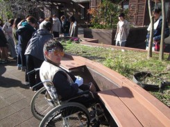高齢者疑似体験キット「うらしま太郎」を装着し、車いすに乗り、座位（座ったまま園芸活動ができる）のレイズドベッドを体験